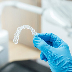 dentist holding clear aligner with blue glove
