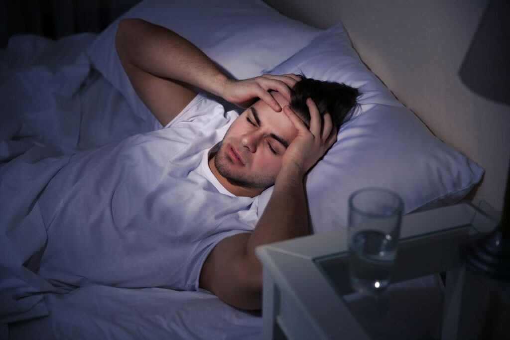 A man lying in bed, holding his head in pain.